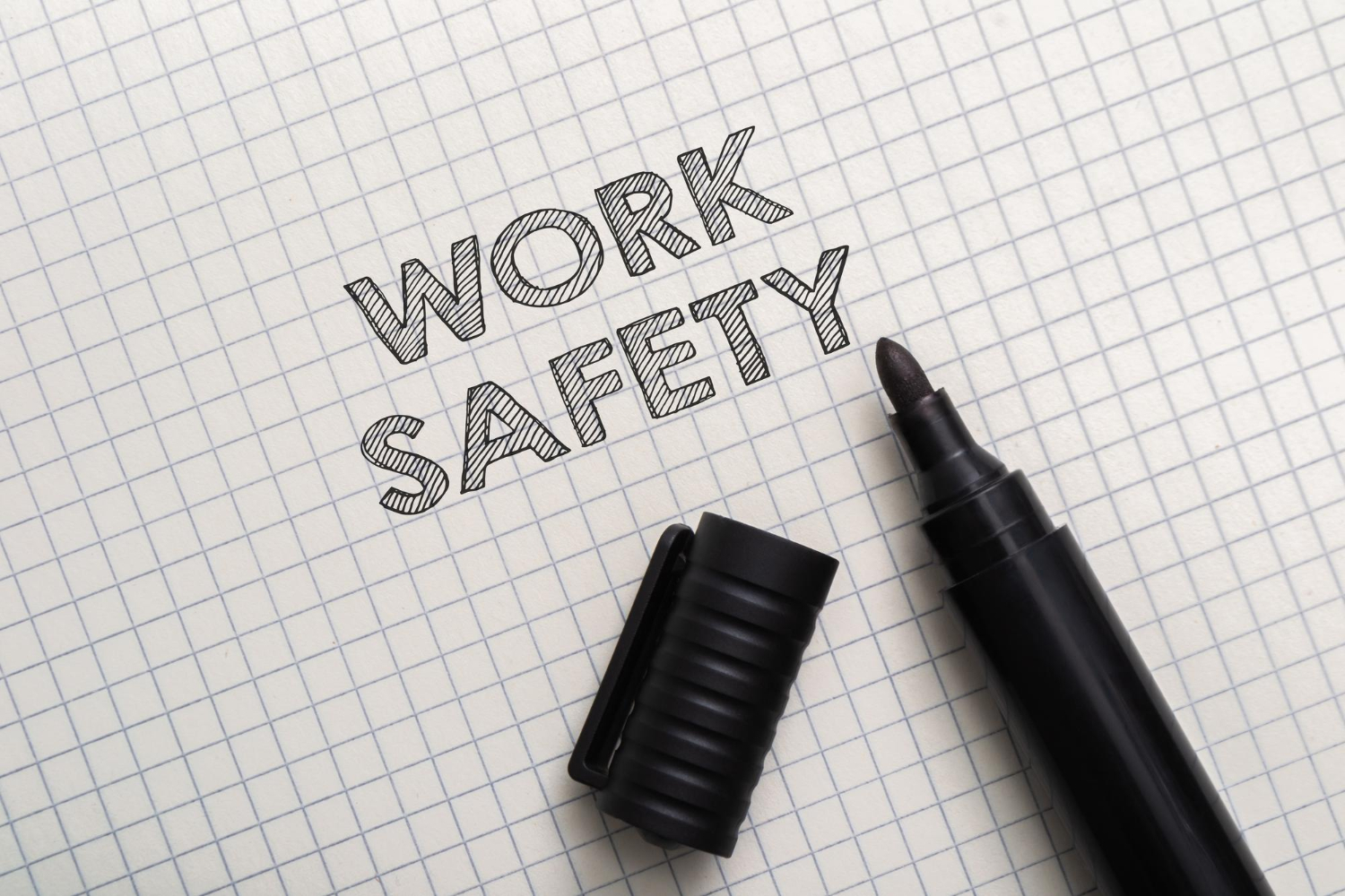 Mots sécurité au travail et marqueur noir ouvert sur papier quadrillé